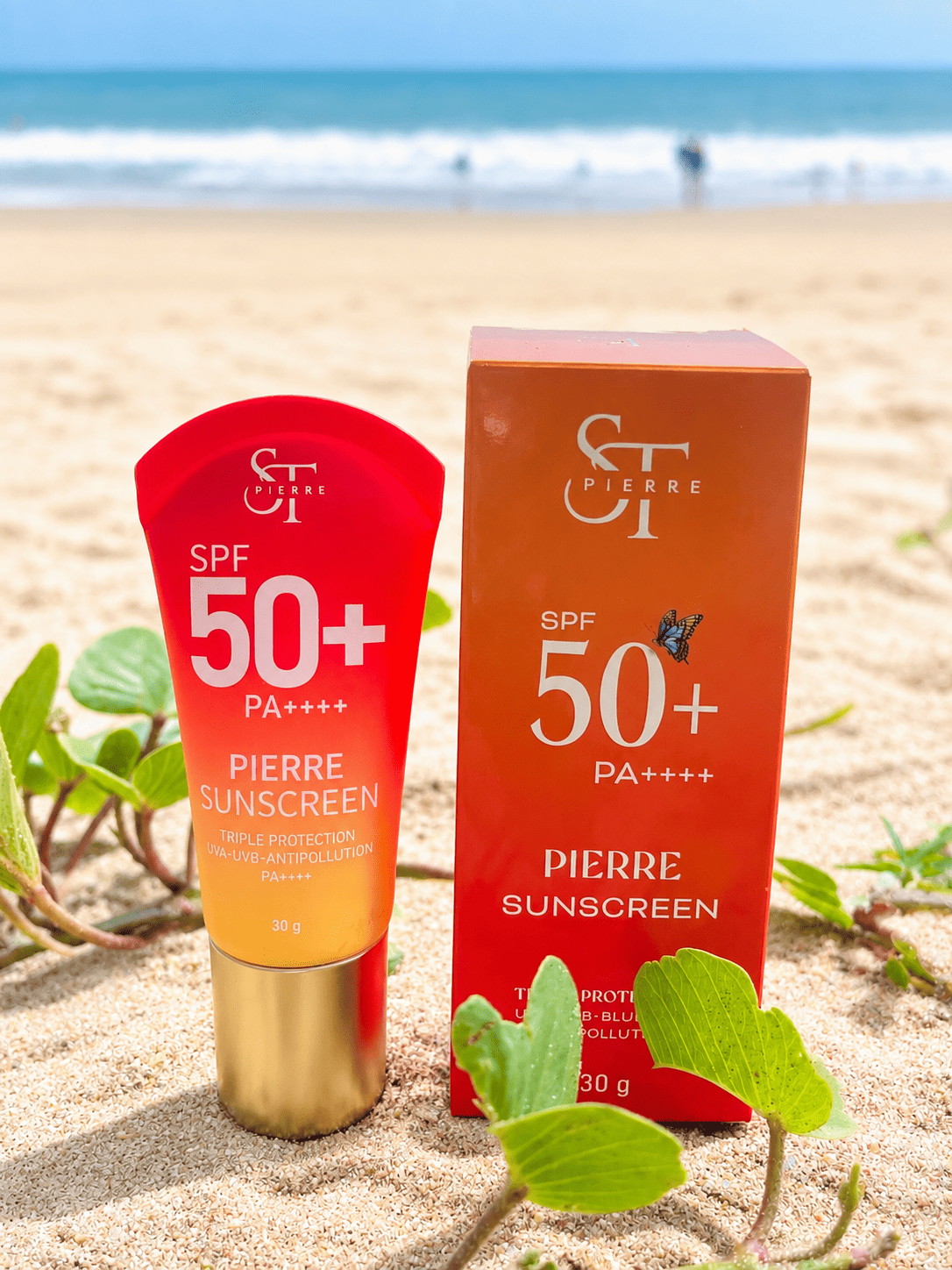 ภาพถ่ายผลิตภัณฑ์ครีมกันแดด Pierre Sunscreen ขนาด 30 กรัม พร้อมกล่องบรรจุภัณฑ์สีส้มวางอยู่บนพื้นทรายริมชายหาด ด้านหลังเห็นวิวทะเลและคลื่น